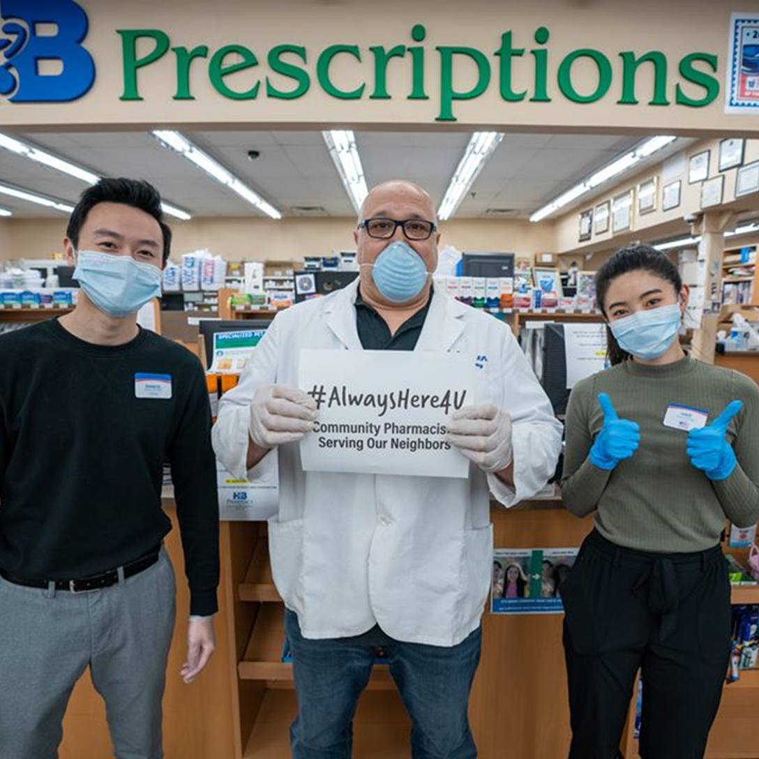 The pharmacists and owner of HB Pharmacy hold up a sign to remind their community they are always there to serve them