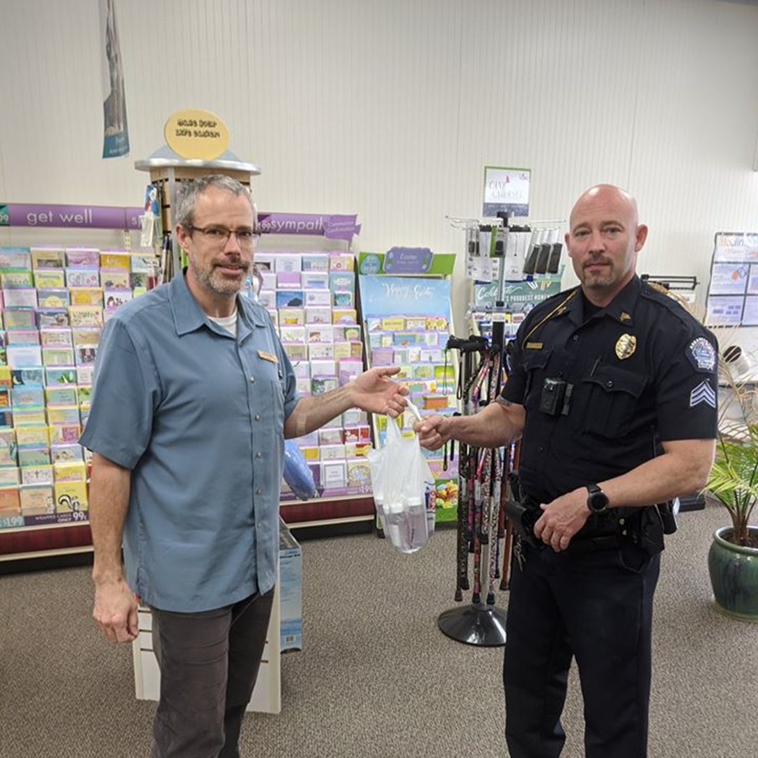 A pharmacist from Taylor Drug hands compounded hand sanitizer to a local police officer