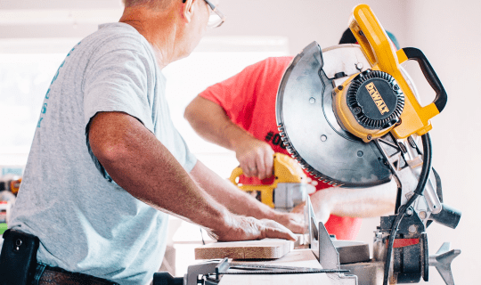 Two men sawing and drilling wood in a pharmacy under construction
