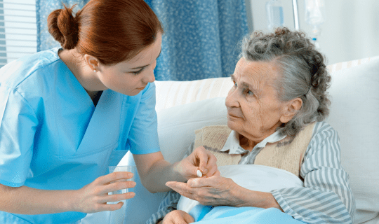 A female nurse handing medication to a woman laying in a hospital bed